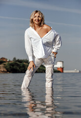 portrait beautiful middle-aged woman in white shirt and trousers on the seashore, concept of youth in adulthood
