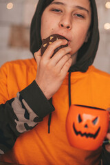 Portrait of candid authentic zoomer boy posing with jack lantern mug and sweets at halloween party