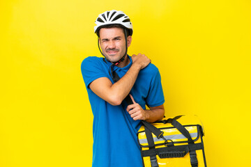 Young handsome man with thermal backpack over isolated yellow background suffering from pain in shoulder for having made an effort