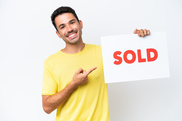 Young handsome man over isolated white background holding a placard with text SOLD and  pointing it