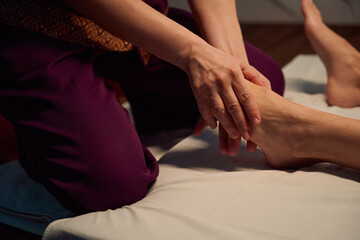 Qualified masseuse giving traditional Thai feet massage to her client