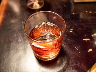 ice cube in alcoholic cocktail with in glass on old bar table illuminated by electric light closeup