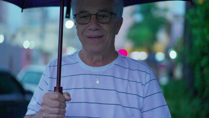 Senior man in the rain holding umbrella. Elderly gray-hair mature caucasian male person walks...