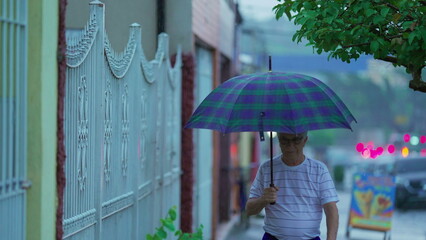 Senior man walking in the rain holding umbrella, older caucasian person strolling in street sidewalk, walks forward in slow-motion, raining season