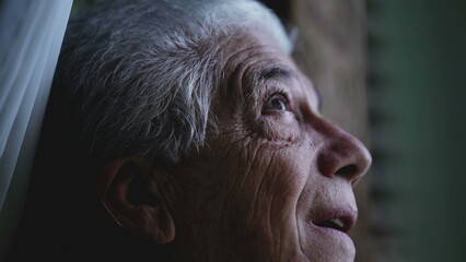 Elderly man close-up face looking up at sky from home window, observing weather and incoming rain. Senior person staring at storm formation