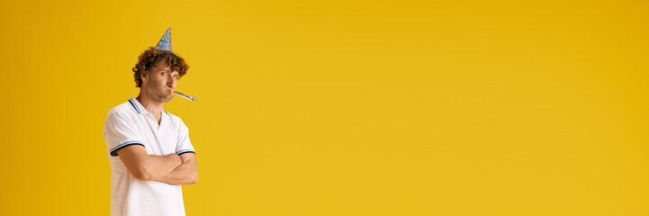 Unpleasant and unhappy mature man celebrating his birthday agsisnt yellow studio background....