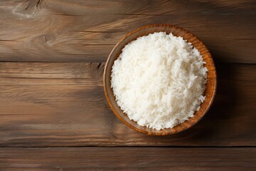Fototapeta na wymiar Bowl of rice on wooden table top. Overhead view.