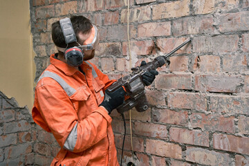 Construction worker using hammer drill with chisel to remove old cement from brick wall indoors,...