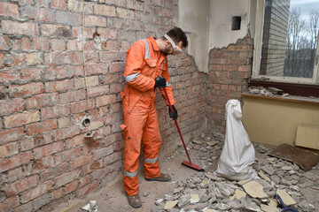 Builder cleaning apartment after demolition jobs, wearing gloves, mask, boots and orange coveralls.