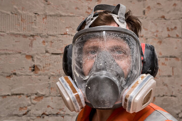 Male worker wearing full face respirator mask and ear defenders for working in hazard environment. 
