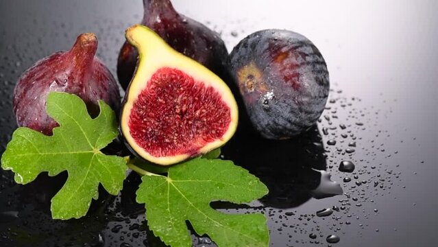 Fig fruits. Ripe sweet figs fruit with leaves close up, on black, gray background. Water drops. Rotating fresh exotic fruits. Slow motion