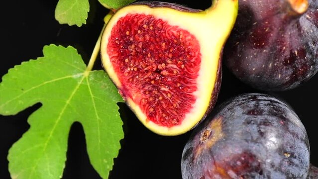 Fig fruits. Ripe sweet fresh figs fruit with leaves close up, rotating on black background , top view. Macro shot