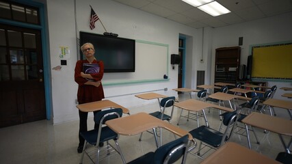 Wide angle view of sad unhappy teacher in large empty classroom with the lights turned off during...