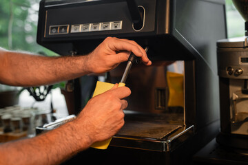 cropped view of barista with rag cleaning coffee machine nozzle while working in coffee shop