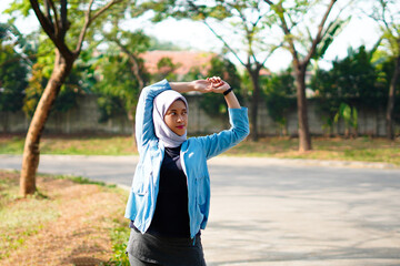 Beautiful Muslim woman working out outdoors in the morning. Sporty woman with a hijab warming up by doing exercises.