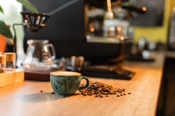 cup of cappuccino near coffee beans on worktop near blurred coffee machine in cafe