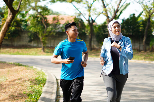 Young muslim couple happy together running at green summer park. Man and woman in hijab doing morning workout outdoors.
