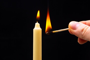 Lighting a candle with a wooden match on a dark background. Burning candle fire