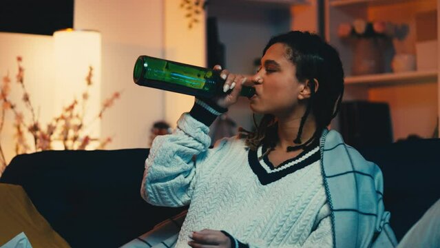Upset lonely African American woman drinking alcohol from bottle, bad mood