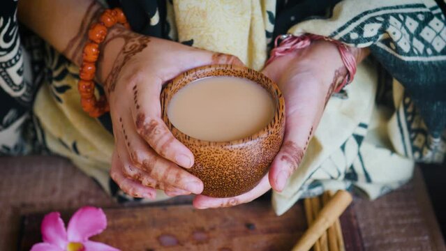 Indian woman hands holding wooden cup of masala chai tea. Close up.