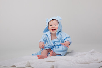 Cute happy laughing baby in a soft bathrobe after bathing plays on a white background. The child is...