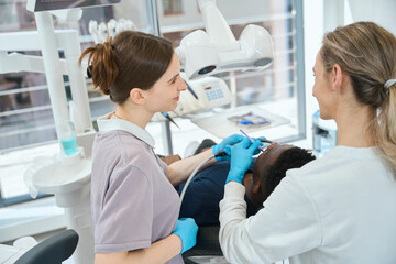 Nurse holding saliva ejector while professional dentist doing treatment