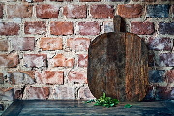 Rustic wooden chopping board against an old brick wall. Culinary background. Copy space