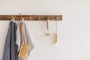 Wood hook rack with tea towels, broom and dish bottle brush hanging on a white wall on the modern...