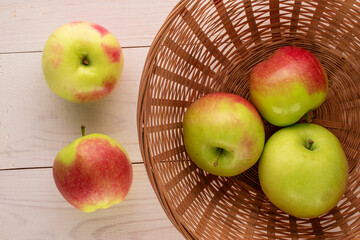 Several green apples with a straw plate on a wooden table, macro, top view.