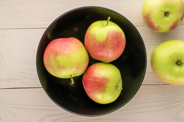 Several green apples with black ceramic plate on wooden table, macro, top view.