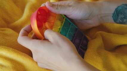 Colorful rainbow antistress sensory toy fidget push pop it on human hand. Young woman plays simple dimple. Rubber multicolored among as character. Trending things popular among children and adults