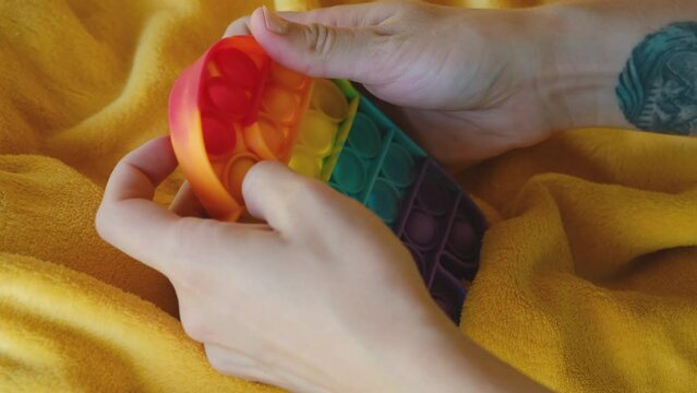 Colorful rainbow antistress sensory toy fidget push pop it on human hand. Young woman plays simple dimple. Rubber multicolored among as character. Trending things popular among children and adults