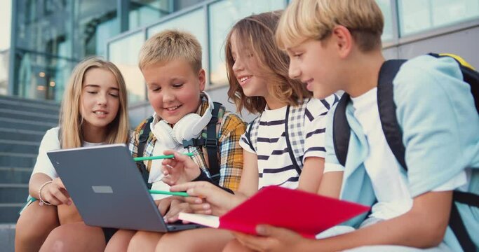 Group of diverse good-looking modern school girls and boys doing a project together with a laptop in a school building background. Concept of learning and lifestyle in teens life.