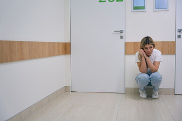 Frightened blonde woman in jeans squatting in the hospital corridor