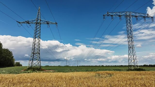 Movement below two high-voltage pylons. Dramatic bottom view of two high voltage power lines. The lines reach to the horizon. Below the masts the field is cultivated with grain and fodder plants.
