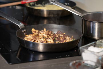 Cooked sliced mushrooms in a pan on electronic stove in kitchen.