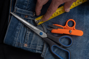 Detail of jeans with scissors and measuring tape: sewing tools on denim fabric