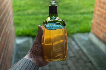 "Whiskey bottle held in hand on a blurred green grass background - warm tone and relaxing atmosphere in a horizontal scene
