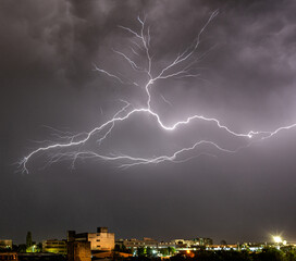 Tree shaped lightning above industrial city area. Night sky with grey clouds over the city. Urban area and electrical discharge. 