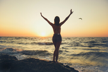 Silhouette of a girl with outstretched arms against the backdrop of dawn over the sea or ocean.