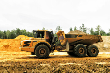 a crawler excavator loads sand into a truck. Large hills and heaps of sand, gravel, crushed stone of yellow, gray and black colors