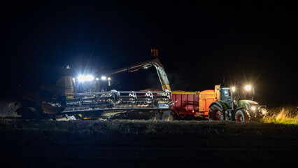 Combine harvester working at night. Offloading rain to a tractor trailer.