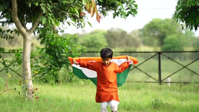 Happy Cute little indian kids holding, waving or running with Tricolour with greenery in the background, celebrating Independence or Republic day