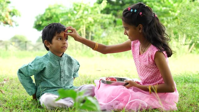 Happy young indian girl tying rakhi to brother hand during raksha bandhan festival at home - concept of indian culture, relationship and occasion