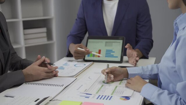 Young businessman, Asian stock trader agent or sales tax credit broker, brief introduction and pointing hand to graph report. Discuss with clients at desks showing budget charts or legal results.