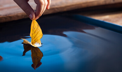 Autumn yellow leaf ship in children hand in water. Boy in park play with boat in river.