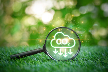 Magnifying glass focused on CO2 emission reduction icons on the grass in garden with green nature...