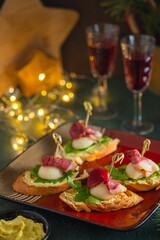 Mini sandwiches with pear, smoked duck and arugula in the shape of a Santa Claus hat on a square plate on a green concrete background. Merry Christmas concept.