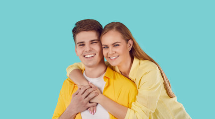 Studio shot of happy family looking at camera and smiling. Young married couple in yellow shirts isolated on turquoise background. Young man with his girlfriend. Pretty woman hugging her boyfriend