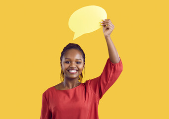 Portrait of smiling African American woman isolated on yellow studio background show mockup speech bubble. Happy African girl demonstrate empty talk balloon with copy space for ad.